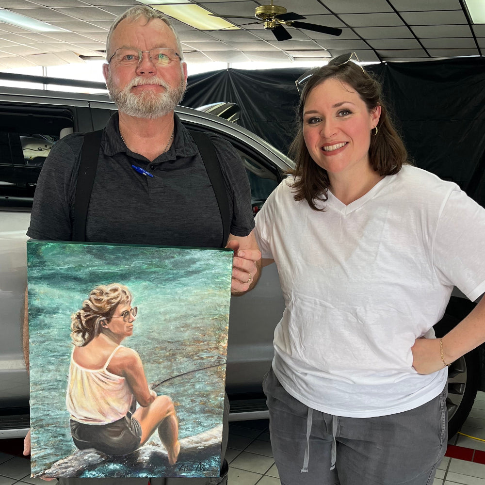 Allison Victoria and collector older gentleman holding commissioned painting a gift for his wife of one of her fishing, warm beige and tan tones and teal and blue water
