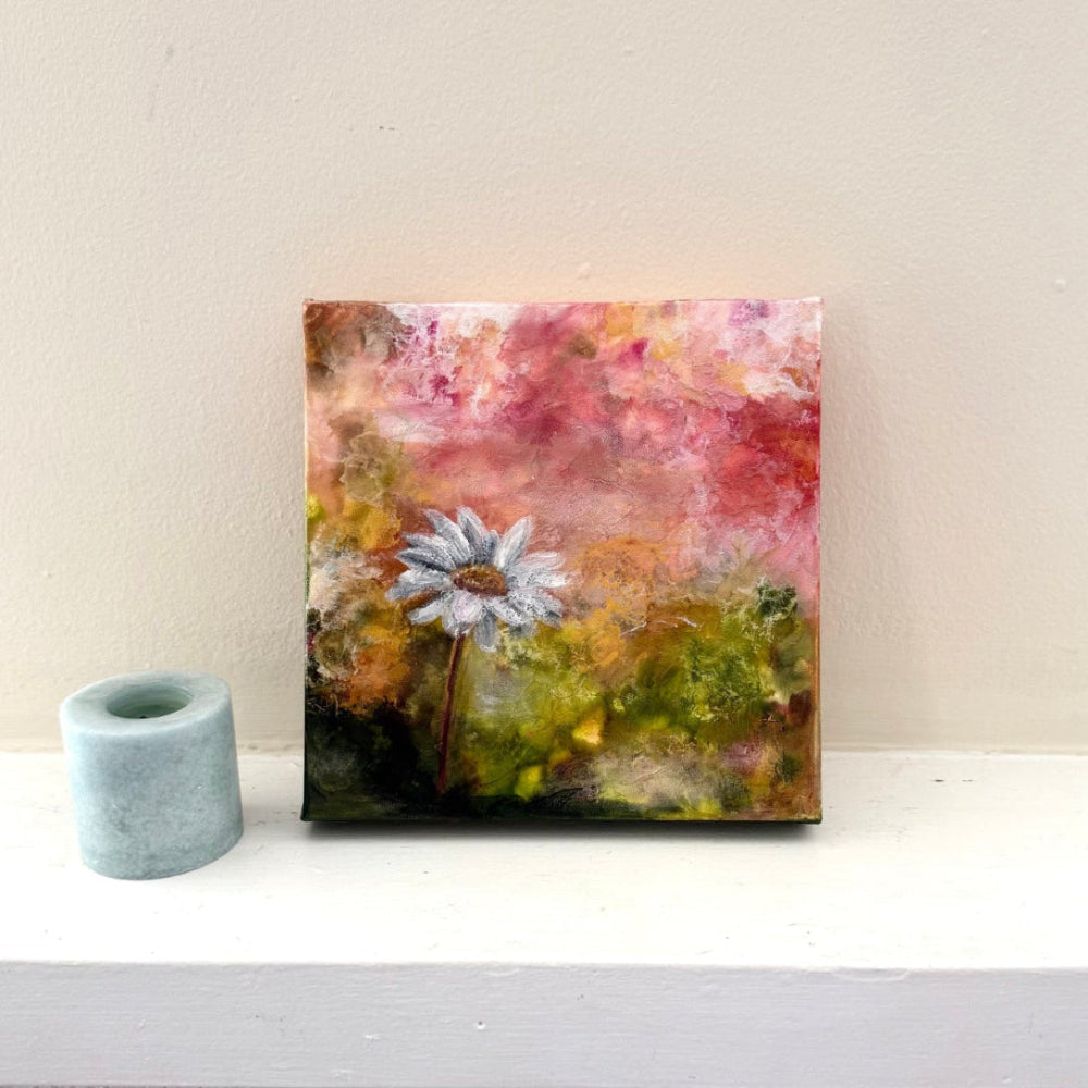 Abstract painting with a flower on a white surface next to a small candle.