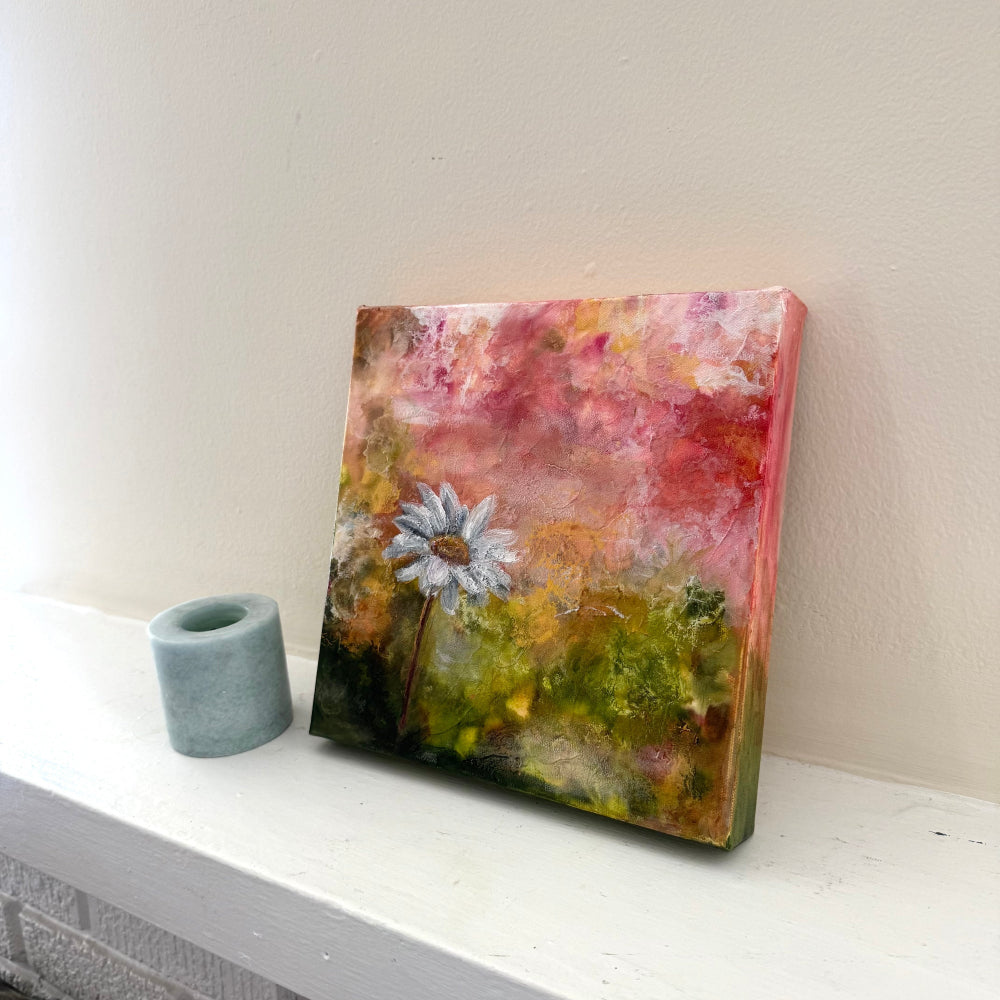 Colorful abstract painting with a white flower on a white surface side angle
