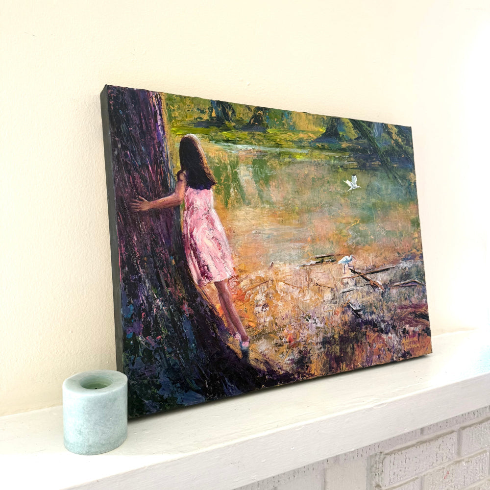 Angled view of a textured acrylic palette knife painting showing canvas depth next to candle, featuring a girl in a pink dress watching birds by the water.