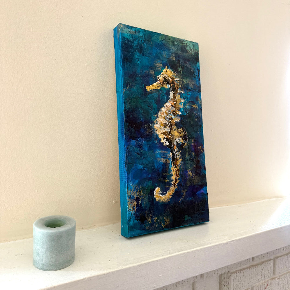 Canvas painting of a seahorse on a textured blue background, displayed on a shelf.