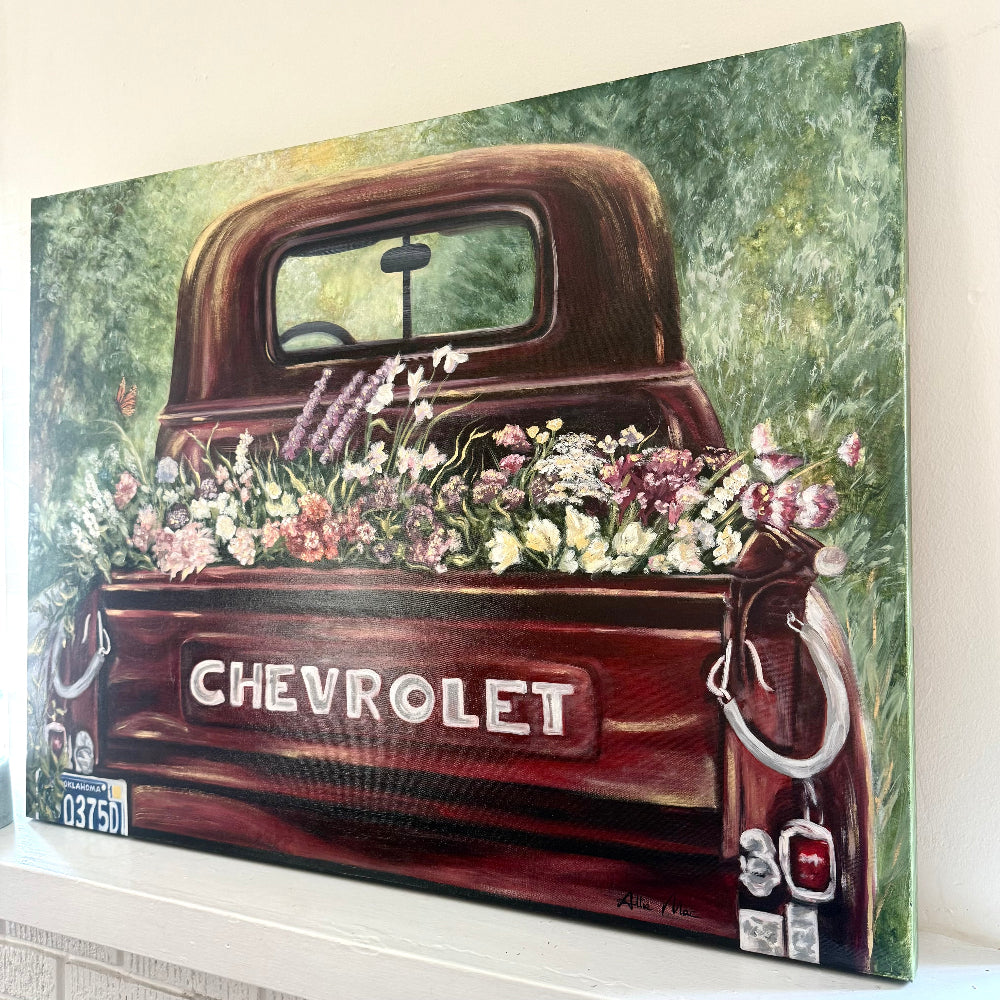 Oil Painting of Old Vintage Red Chevrolet truck with a variety of flowers in the bed on a decorative mantle piece next to a candle, lots of Reds, pinks, and green background