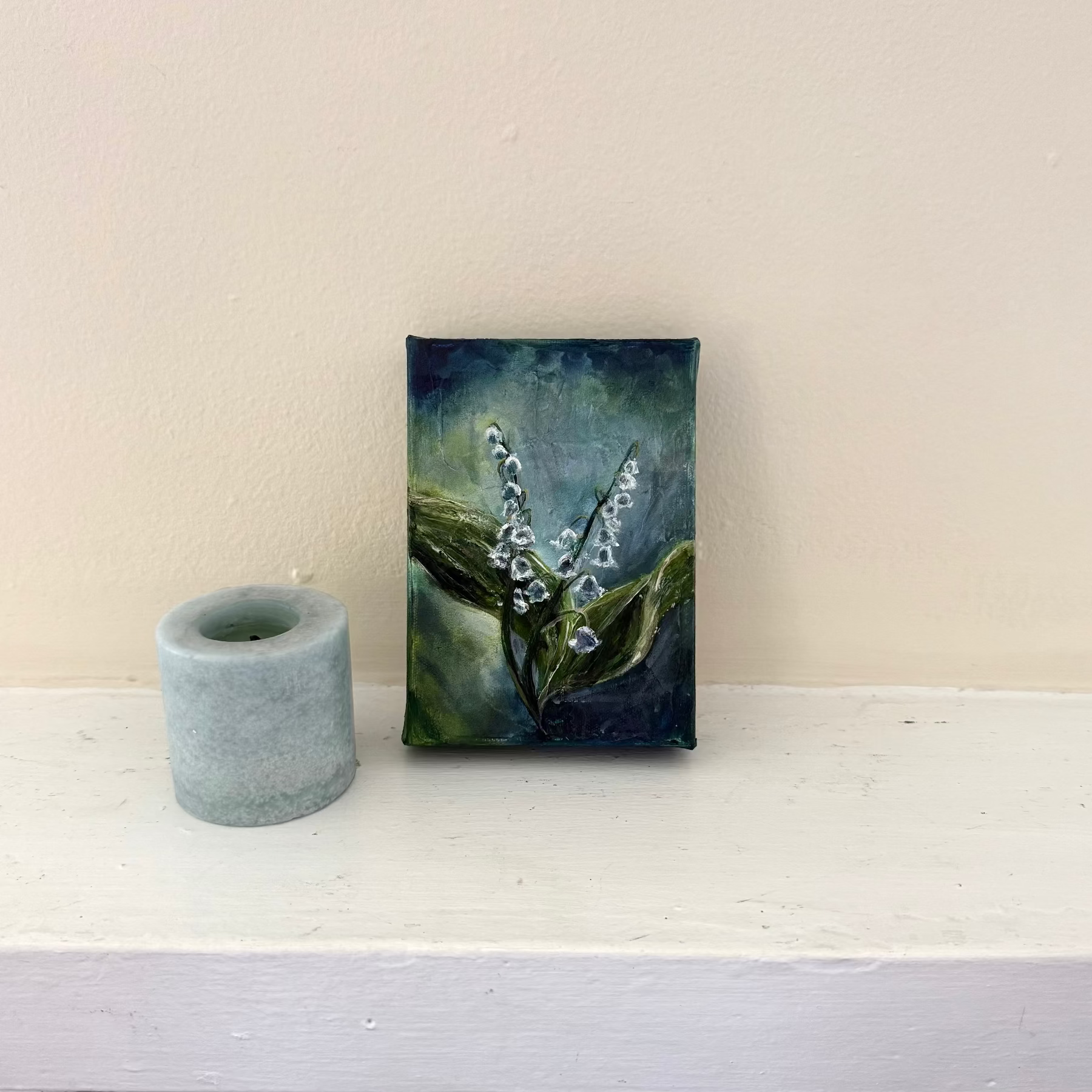 Lily of the Valley flower floral acrylic palette knife painting by Allison Victoria deep greens and blues cool colors on gallery wrapped canvas styled delicately next to a blue candle on a neutral mantle home decor