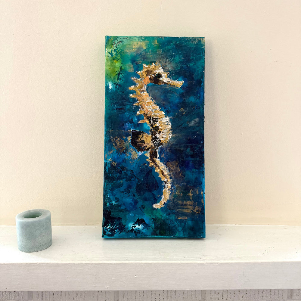 Abstract painting of a seahorse on a blue and green background with a candle beside it.