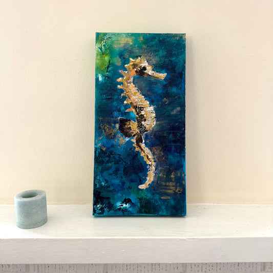 Abstract painting of a seahorse on a blue and green background with a candle beside it.