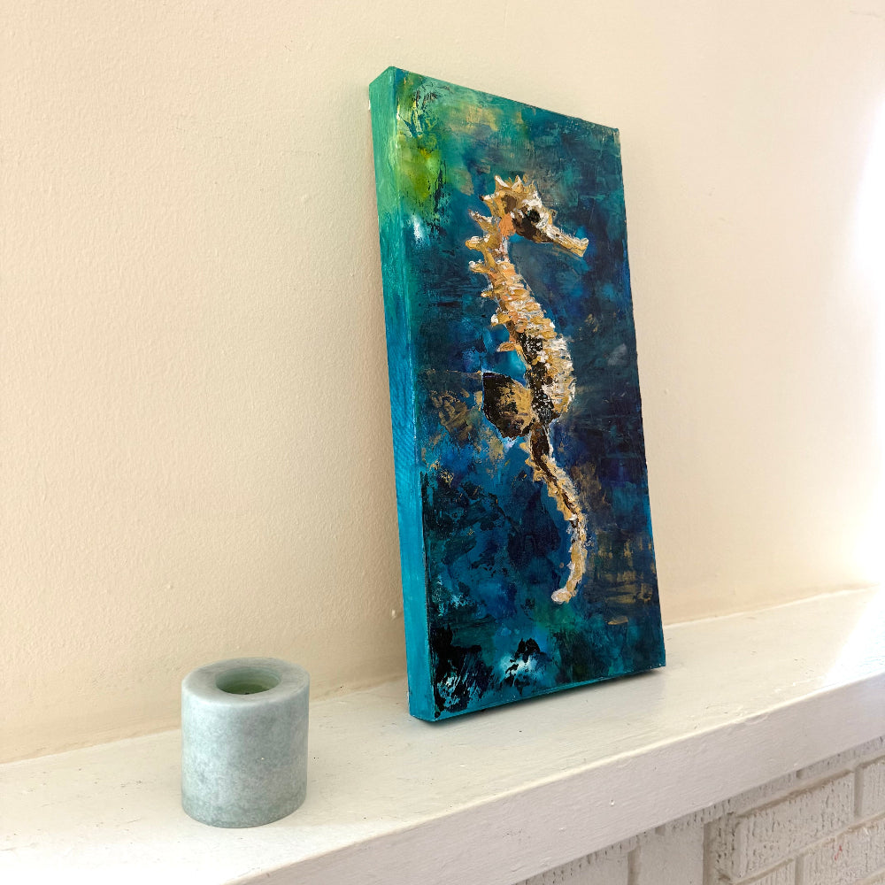 Abstract painting of a seahorse on a textured surface with a candle beside it.