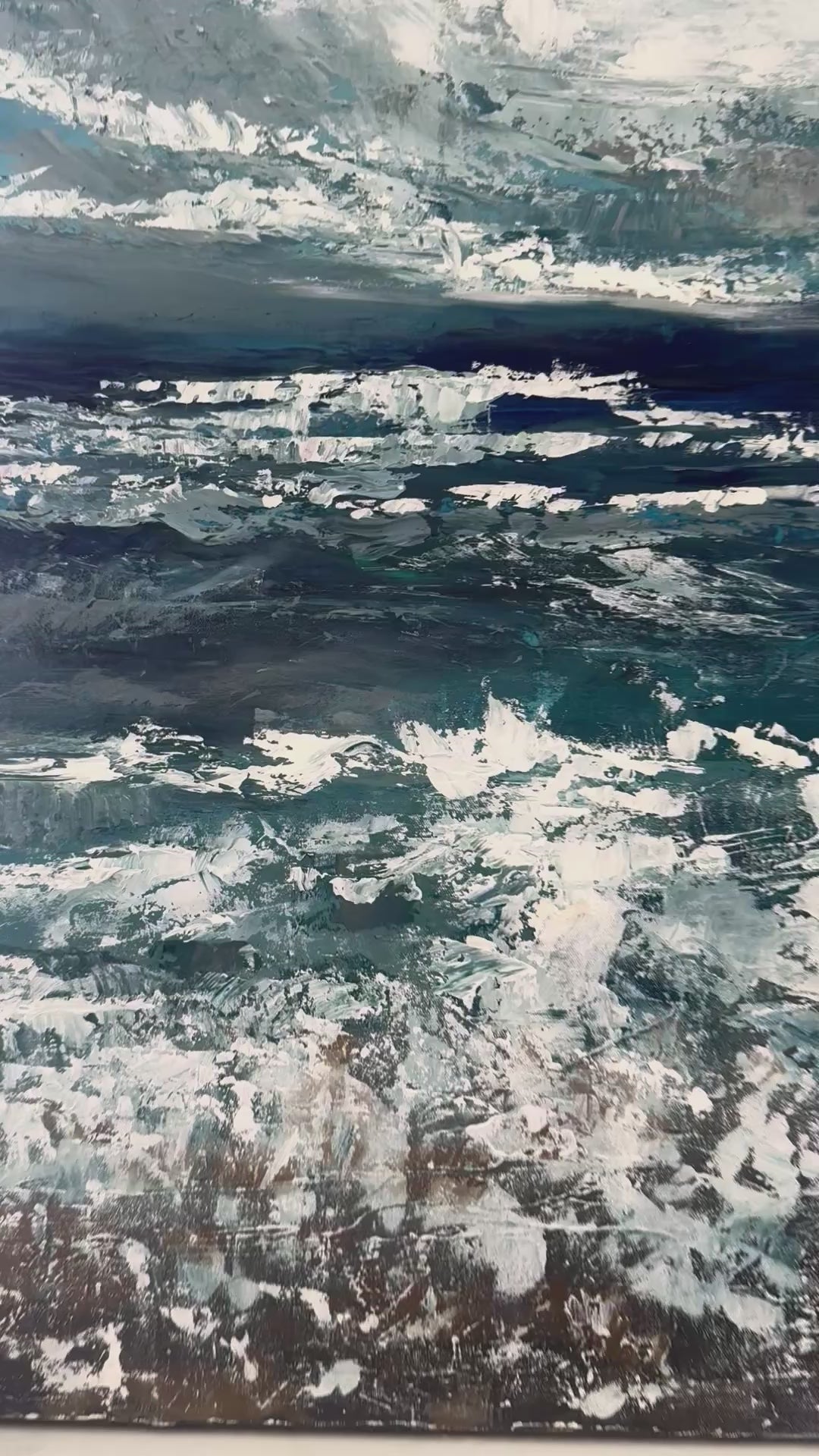 close up of large acrylic palette knife ocean painting of deep blues and greys and whites and browns that zooms out to show the whole painting resting on top of a light white neutral background