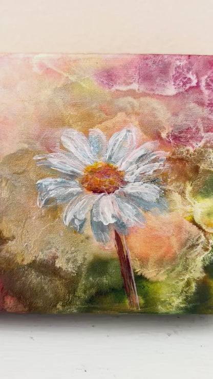 Video up close to daisy flower of small painting with abstract pinks gold and green background zooms out to show the painting on lgiht white neutral background