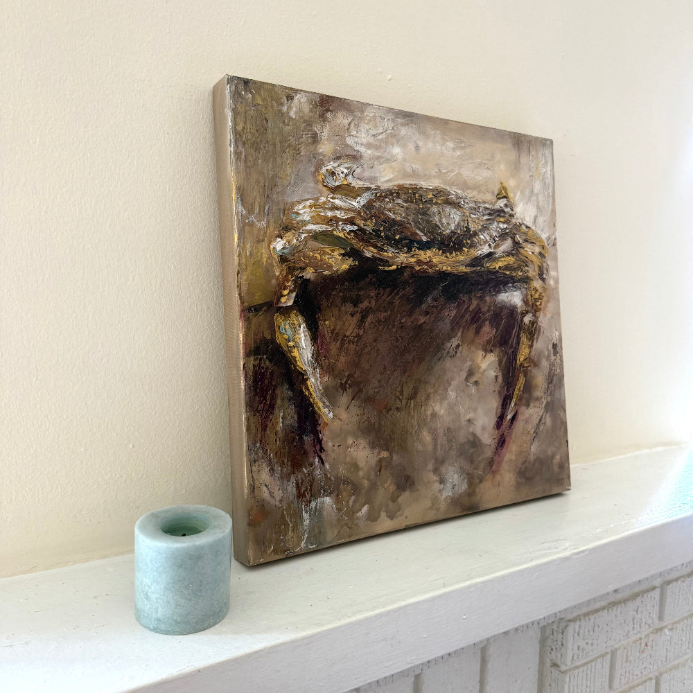 Abstract coastal crab acrylic palette knife painting with gold and brown tones on a white shelf against a light wall.